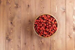 rot Hunderose Hagebutte Früchte im ein hölzern Schüssel auf hölzern Tabelle foto