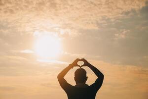 Hand Herz Rahmen gestalten Silhouette gemacht gegen das Sonne Himmel von ein Sonnenaufgang oder Sonnenuntergang auf foto