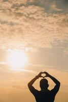 Hand Herz Rahmen gestalten Silhouette gemacht gegen das Sonne Himmel von ein Sonnenaufgang oder Sonnenuntergang auf foto