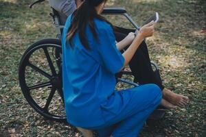 Alten asiatisch Senior Frau auf Rollstuhl mit asiatisch Vorsichtig Pflegekraft und ermutigen geduldig, Gehen im Garten. mit Pflege von ein Pflegekraft und Senior Gesundheit Versicherung im Sonne Licht foto