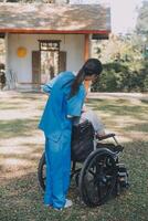jung asiatisch Pflege Helfer mit Asien Alten Frau auf Rollstuhl entspannen zusammen Park draußen zu Hilfe und ermutigen und sich ausruhen Ihre Verstand mit Grün Natur. Hilfe Unterstützung du selber zu lernen zu gehen. Gehhilfe foto