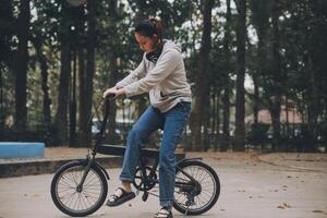 glücklich asiatisch jung Frau gehen und Reiten Fahrrad im Park, Straße Stadt ihr lächelnd mit Fahrrad von Transport, Öko freundlich, Menschen Lebensstil Konzept. foto