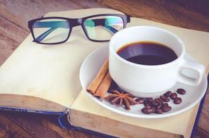 Buch Brille und Tasse von Kaffee auf Holz beim Morgen foto