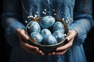 ai generiert ein Schüssel voll von gemalt Blau Ostern Eier und wenig Zweige im das Hände von ein Frau im ein Jahrgang National Blau Kostüm foto