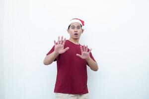 jung asiatisch Mann tragen ein Santa claus Hut ausdrücken Schock und Unwilligkeit isoliert durch ein Weiß Hintergrund zum visuell Kommunikation foto