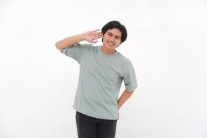 ein jung asiatisch Mann, ein Mitarbeiter im ein T-Shirt, ist gesehen begeistert Hören mit seine Hand zu seine Ohr gegen ein Weiß Hintergrund. foto