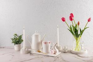 stilvoll immer noch Leben zum das Ostern Urlaub. Weiß Kaffee Topf auf Keramik Weiß Tablett mit Becher, Ostern Hase Zahlen. Vase von Blumen und Kerzen. foto