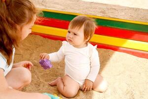 Baby Mädchen zum das zuerst Zeit im das Sandkasten sieht aus vorsichtig beim ihr älter Schwester foto