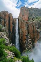 ai generiert Magier erfasst mächtig Wasserfall Kaskadierung Nieder robust, felsig Berg Cliff. das Himmel über ist teilweise wolkig Anzeige Leben inmitten das felsig Terrain ai generiert foto