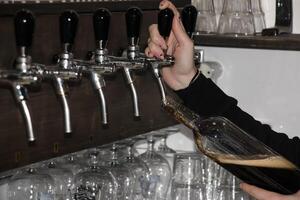 hinter das Schalter. Damen Hände schön und leicht gießen Bier in ein Flasche. foto