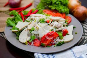 würzig Glas Nudel Salat mit Vietnamesisch Würstchen serviert im ein grau Teller stellen auf ein hölzern Tabelle und verschiedene Gemüse. foto