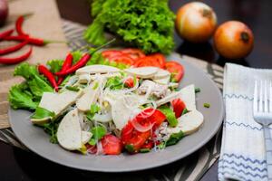 würzig Glas Nudel Salat mit Vietnamesisch Würstchen serviert im ein grau Teller stellen auf ein hölzern Tabelle und verschiedene Gemüse. foto