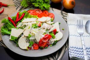 würzig Glas Nudel Salat mit Vietnamesisch Würstchen serviert im ein grau Teller stellen auf ein hölzern Tabelle und verschiedene Gemüse. foto