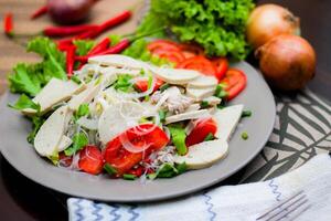 würzig Glas Nudel Salat mit Vietnamesisch Würstchen serviert im ein grau Teller stellen auf ein hölzern Tabelle und verschiedene Gemüse. foto