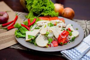 würzig Glas Nudel Salat mit Vietnamesisch Würstchen serviert im ein grau Teller stellen auf ein hölzern Tabelle und verschiedene Gemüse. foto