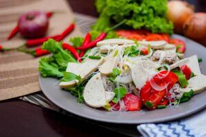 würzig Glas Nudel Salat mit Vietnamesisch Würstchen serviert im ein grau Teller stellen auf ein hölzern Tabelle und verschiedene Gemüse. foto