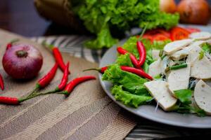 würzig Glas Nudel Salat mit Vietnamesisch Würstchen serviert im ein grau Teller stellen auf ein hölzern Tabelle und verschiedene Gemüse. foto