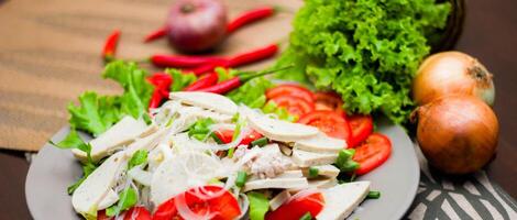 würzig Glas Nudel Salat mit Vietnamesisch Würstchen serviert im ein grau Teller stellen auf ein hölzern Tabelle und verschiedene Gemüse. foto