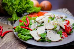 würzig Glas Nudel Salat mit Vietnamesisch Würstchen serviert im ein grau Teller stellen auf ein hölzern Tabelle und verschiedene Gemüse. foto