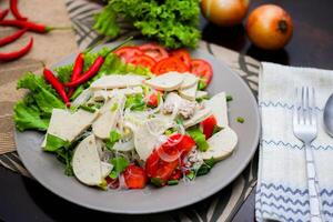 würzig Glas Nudel Salat mit Vietnamesisch Würstchen serviert im ein grau Teller stellen auf ein hölzern Tabelle und verschiedene Gemüse. foto