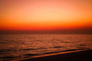 das Meer nach Sonnenuntergang hat ein Orange glühen und ein Orange Himmel mit Nein Wolken. foto