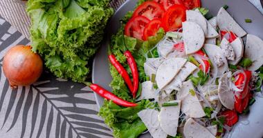 würzig Glas Nudel Salat mit Vietnamesisch Würstchen serviert im ein grau Teller stellen auf ein hölzern Tabelle und verschiedene Gemüse. foto