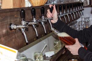 hinter das Schalter. Damen Hände schön und leicht gießen Bier in ein Flasche. foto