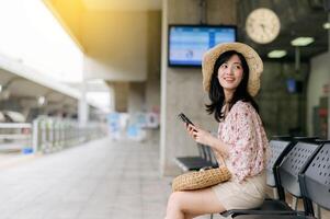 jung asiatisch Frau Reisender mit Weberei Korb mit ein Handy, Mobiltelefon Telefon und warten zum Zug im Zug Bahnhof. Reise Ausflug Lebensstil, Welt Reise Forscher oder Asien Sommer- Tourismus Konzept. foto