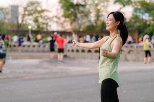 weiblich Jogger. passen jung asiatisch Frau mit Grün Sportbekleidung Aerobic tanzen Übung im Park und genießen ein gesund draussen. Fitness Läufer Mädchen im Öffentlichkeit Park. Wellness Sein Konzept foto