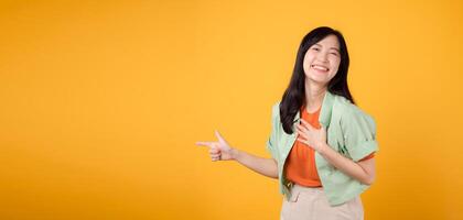 jung asiatisch Frau im ihr 30er Jahre tragen ein Grün Hemd auf ein Orange Shirt, zeigen Finger zu kostenlos Kopieren Raum. erkunden das Welt von Rabatt Einkaufen Beförderung Konzept. foto