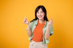 schön jung asiatisch Frau im ihr 30er Jahre zeigen ein Mini Herz Finger Geste, ausdrücken Zuneigung mit sanft lächeln. Konzept von Körper Sprache wie sie posiert drinnen tragen ein Orange Hemd und Grün Jumper. foto