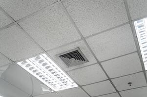 Deckenmontierte Kassettenklimaanlage und modernes Lampenlicht an weißer Decke. Kanalklimagerät für Haus, Flur oder Büro. foto