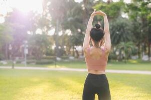 Wellness und gesund Lebensstil Porträt 30er Jahre asiatisch Frau im Rosa Sportbekleidung. vorbereiten und Dehnen Arm Muskeln Vor Sonnenuntergang Lauf im das Park. Fitness draußen und Umarmung ausgewogen Leben. foto