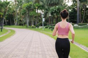 Frau Jogger. zurück Perspektive Porträt von jung asiatisch weiblich tragen Rosa Sportbekleidung Laufen im Öffentlichkeit Park. Gesundheitswesen Wellness Konzept. foto