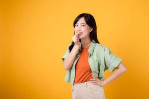 Umarmung Glück mit ein jung asiatisch Frau im ihr 30er Jahre, gekleidet im ein Orange Hemd und Grün Jumper. ihr Mini Herz Geste, Hüfte halten, und sanft Lächeln vermitteln ein tiefgreifend Botschaft durch Körper Sprache. foto