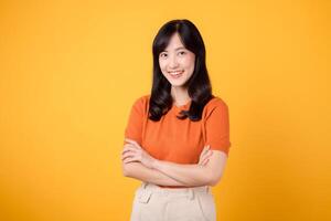verkörpern Vertrauen und Haltung mit ein jung asiatisch Frau im ihr 30er Jahre, anziehen ein Orange Shirt, präsentieren gekreuzt Arm Zeichen Geste auf Gelb Hintergrund. foto