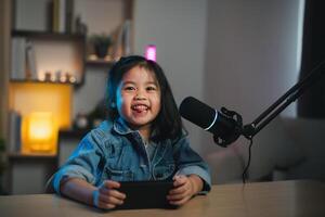 asiatisch Influencer jung Mädchen Lächeln heiter mit Handy, Mobiltelefon Telefon spielen Spiel Leben Streaming Gruß Video Konferenz mit Laptop und tragen Kopfhörer. Kinder Streaming Besetzung Spiel online Konzept. foto