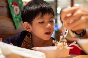 ein wenig asiatisch Junge ist Essen während seine Mutter Einspeisungen ihn. foto