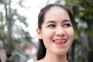 Porträt von ein jung asiatisch Frau mit Hosenträger auf ihr Zähne foto