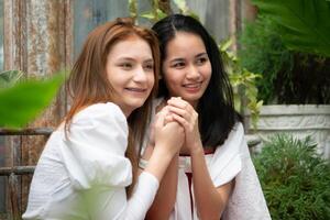zwei jung asiatisch Frauen im rot und Weiß Kleider Sitzung auf ein hölzern Bank im das Garten. foto
