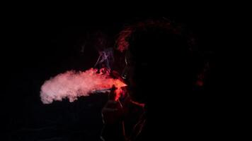 Mann mit ein Zigarette im seine Hand, weht Rauch aus von seine Mund gesehen im Profil im Silhouette mit rot Licht leuchten seine Profil gegen schwarz Hintergrund foto