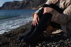 Nahansicht Schuss. weiblich Hände umarmen Knie Sitzung auf das Strand foto