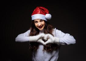 ein Frau im ein Santa Hut Herstellung ein Herz mit ihr Hände. ein froh Frau Verbreitung Liebe und jubeln foto