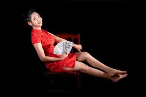 Porträt asiatische Frau rotes Kleid traditionelles Cheongsam hält Geld 100-US-Dollar-Scheine auf schwarzem Hintergrund