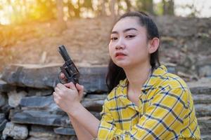 Porträt der Bauer-Asea-Frau, die eine gelbe Hemdhand trägt, die eine alte Revolverpistole auf dem Bauernhof hält, junges Mädchen mit einer Pistole im Garten foto