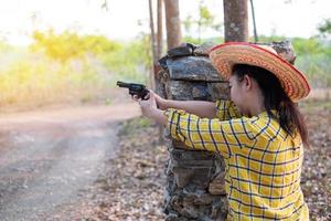 Porträt der Bauer-Asea-Frau, die einen Hut beim Schießen aus einer alten Revolverpistole auf der Farm trägt, junges Mädchen, das in der Haltung sitzt, zu zielen und durch die Visierpistole zu schauen foto