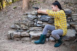 Porträt der Bauer-Asea-Frau, die einen Stiefel beim Schießen aus einer alten Revolverpistole auf der Farm trägt, junges Mädchen, das in der Haltung sitzt, zu zielen und durch die Visierpistole zu schauen foto