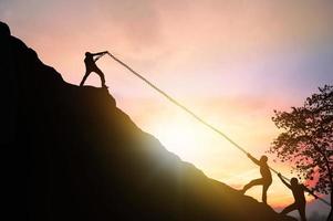 Silhouette des Erfolgs, Business-Teamwork und Motivationskonzept, Leute ziehen Freunde und helfen beim Wandern auf dem Berg