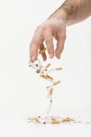 Nahaufnahme der Hand, die zerbrochene Zigaretten vor weißem Hintergrund wirft