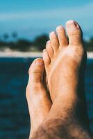 Nahansicht von ein entspannend barfuß mit Zehen oben gegen ein sonnig Strand Hintergrund und Flip Flop bräunen Markierungen foto